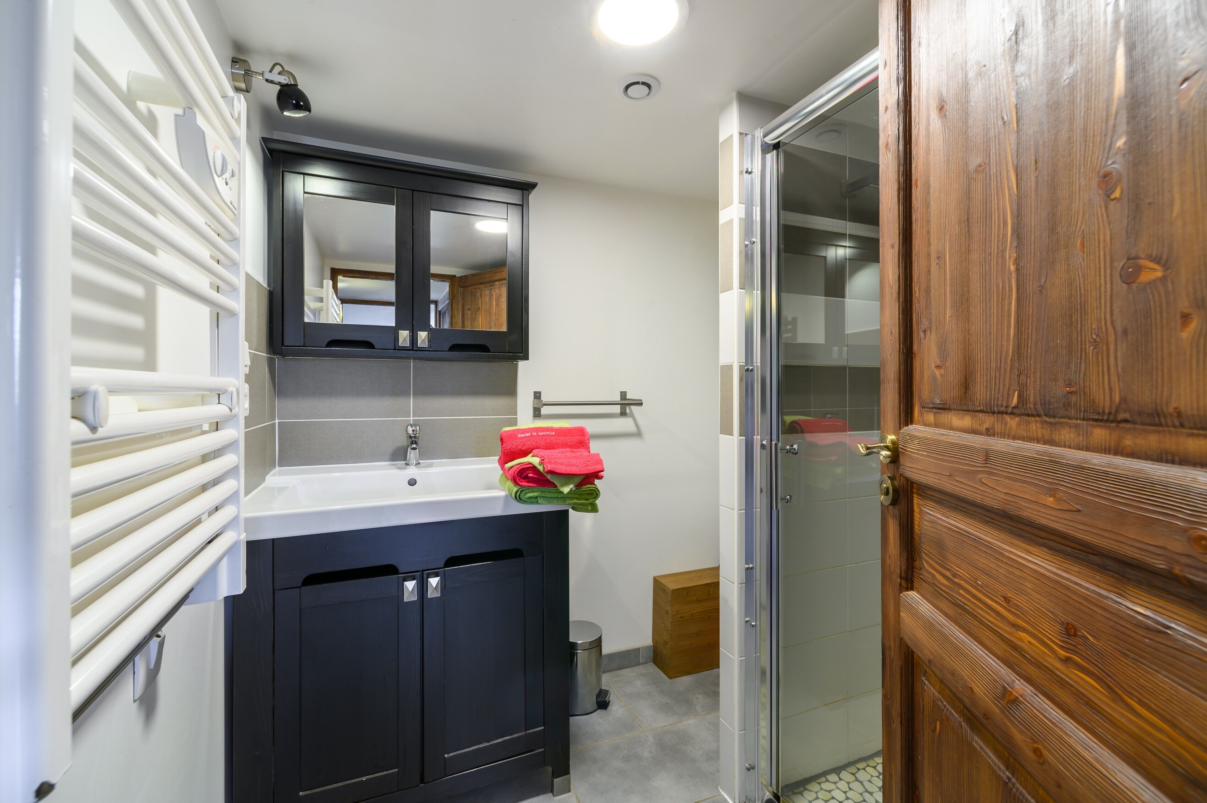 Une salle de bain avec un lavabo, un miroir, un porte-serviettes et une porte en bois.