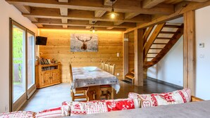 Ein Holzinnenraum mit einem Esstisch, Stühlen, einer Couch, einer Treppe und einem Bild von einem Reh.