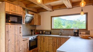 Eine Küche mit Holzausstattung, einem Einbauofen, einer Mikrowelle, einem Toaster und einem großen Fenster mit Blick ins Grüne.