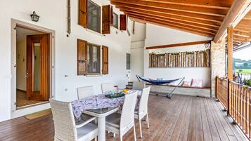 Une terrasse couverte avec une table en bois et des chaises en osier, un hamac et une vue sur l’extérieur.