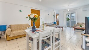 A living room with a white table, beige sofa, and a TV on a stand. - Eftichia Nea Chora Apartment with Mountain View, Shared Garden & Wi-Fi (Chania)