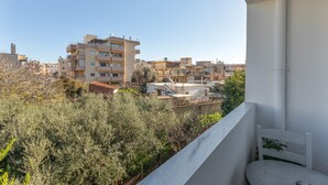A balcony with a white chair, overlooking a residential area with multi-story buildings and dense vegetation. - Eftichia Nea Chora Apartment with Mountain View, Shared Garden & Wi-Fi (Chania)