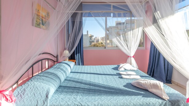 A room with a bed, a window with a view of buildings, and a mosquito net. - Eftichia Nea Chora Apartment with Mountain View, Shared Garden & Wi-Fi (Chania)