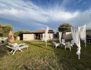 Un jardin avec une pergola, des chaises blanches et un parasol en chaume.