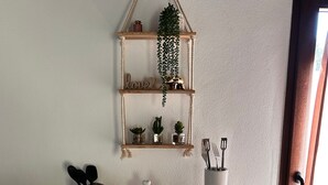 Een aanrecht met een geweven placemat, een hangende plant en potten op een plank.