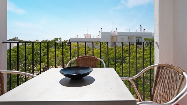Ein Balkon mit Tisch und Stühlen, eine Schale auf dem Tisch und Blick auf Gebäude und Bäume.