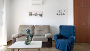 Ein Wohnzimmer mit einem beigen Sofa, einem blauen Sessel, einem weißen Couchtisch und einem Holzschrank.