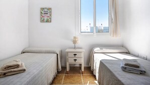 Ein Schlafzimmer mit zwei Betten, einem Nachttisch, einer Lampe, einem Fenster mit Vorhängen und einem Wandbild.