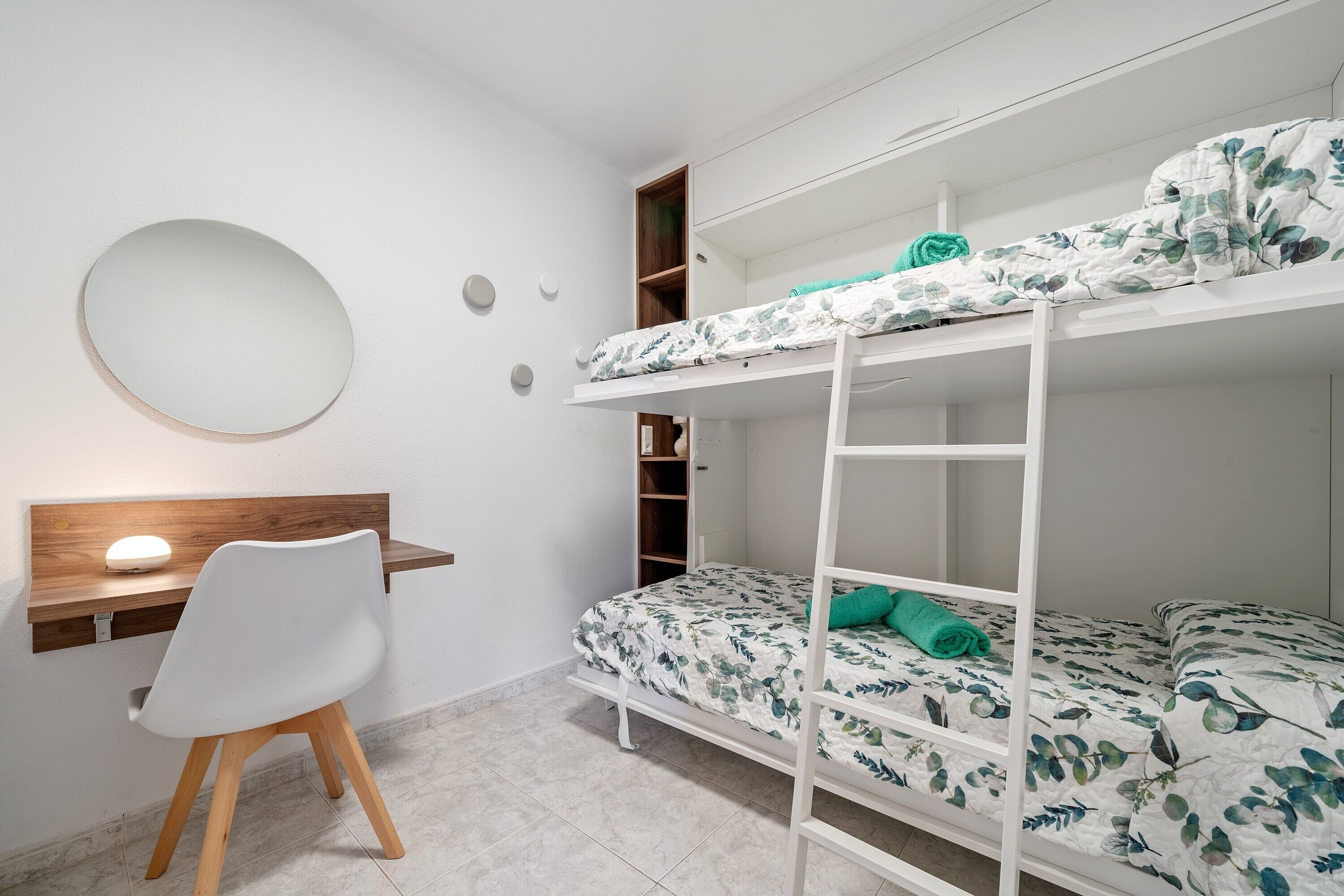 A bunk bed with a desk and chair, a round mirror, and a small shelf unit.