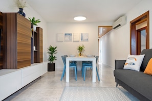 A modern living room with a dining area, a grey sofa, and a white table with blue chairs.