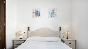 A neatly made bed with white linens, two bedside tables with lamps, and two wall-mounted artworks. - Apartment 'Casa Mar' with Balcony, Wi-Fi and Air Conditioning (Conil de la Frontera)