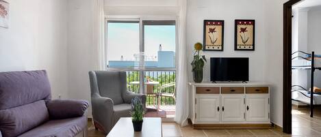 A living room with a sofa, armchair, TV, and a balcony with a view.