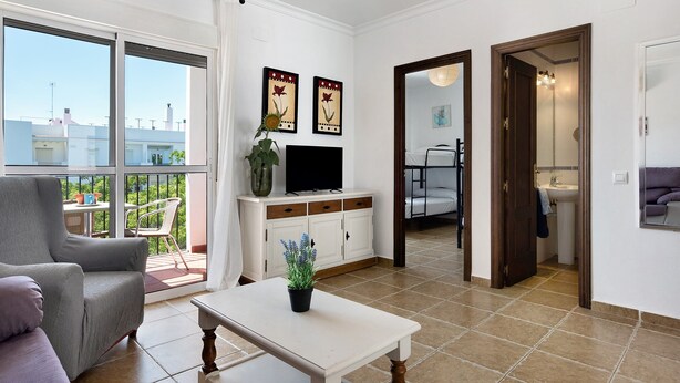 A modern living room with a sofa, a coffee table, a TV, and a balcony with a view of buildings. - Apartment 'Casa Mar' with Balcony, Wi-Fi and Air Conditioning (Conil de la Frontera)