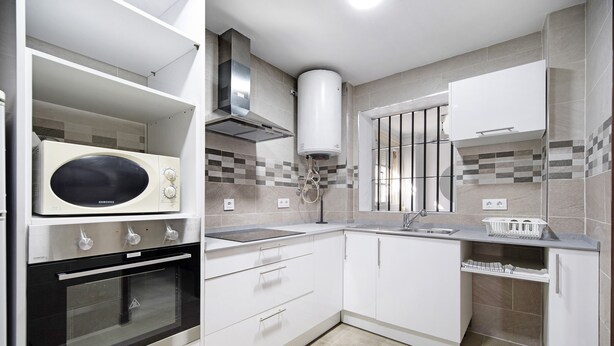 A modern kitchen with white cabinets, a built-in oven, a microwave, and a stainless steel range hood. - Vacation Apartment "Dúplex Chanca" with Private Terrace (El Puerto de Sta María)