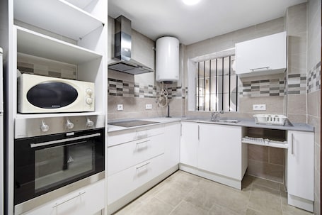 A modern kitchen with white cabinets, a built-in oven, a microwave, and a stainless steel range hood.. Vacation Apartment "Dúplex Chanca" with Private Terrace