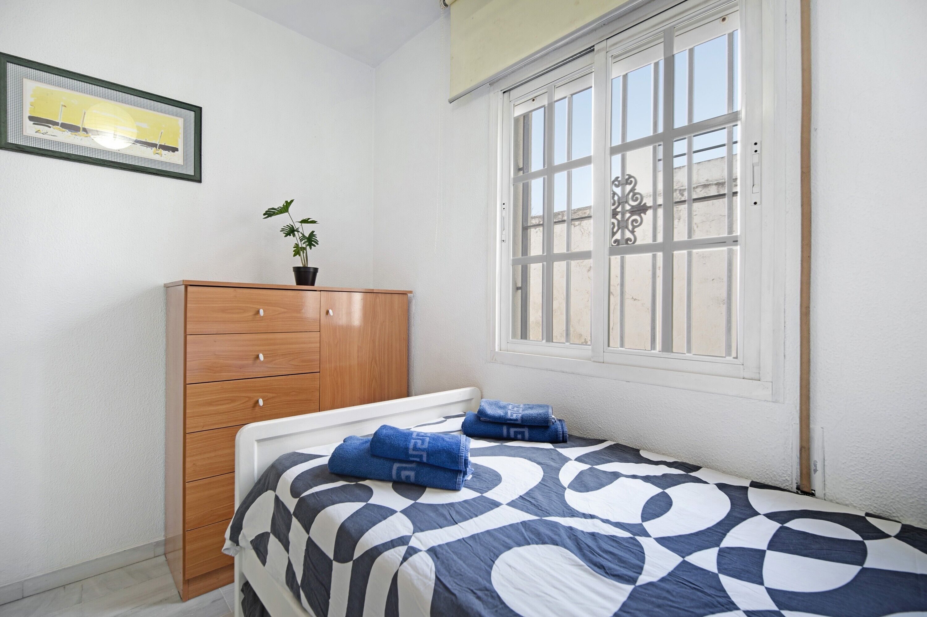 Ein Schlafzimmer mit einem Bett, einer Holzkommode, einem Fenster mit Blick und einem gerahmten Bild an der Wand.