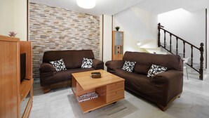 A living room with two brown sofas, a wooden coffee table, a TV stand, and a staircase. - Vacation Apartment "Dúplex Chanca" with Private Terrace (El Puerto de Sta María)