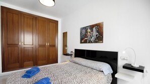 A bedroom with a bed, wooden wardrobe, artwork, bedside table, and a desk lamp. - Vacation Apartment "Dúplex Chanca" with Private Terrace (El Puerto de Sta María)