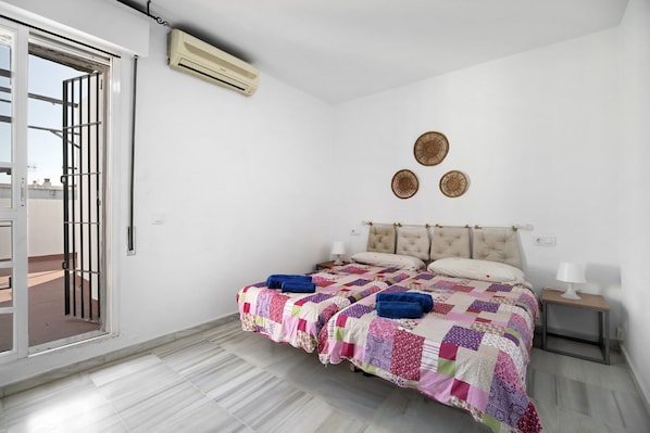 A bedroom with a bed, two bedside tables, an air conditioning unit, and a sliding glass door.