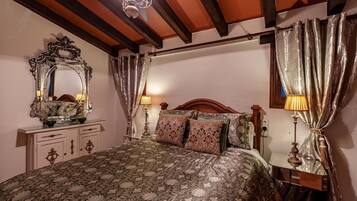 A bedroom with a patterned bedspread, a wooden headboard, a nightstand with a lamp, a dresser with a mirror, and curtains.