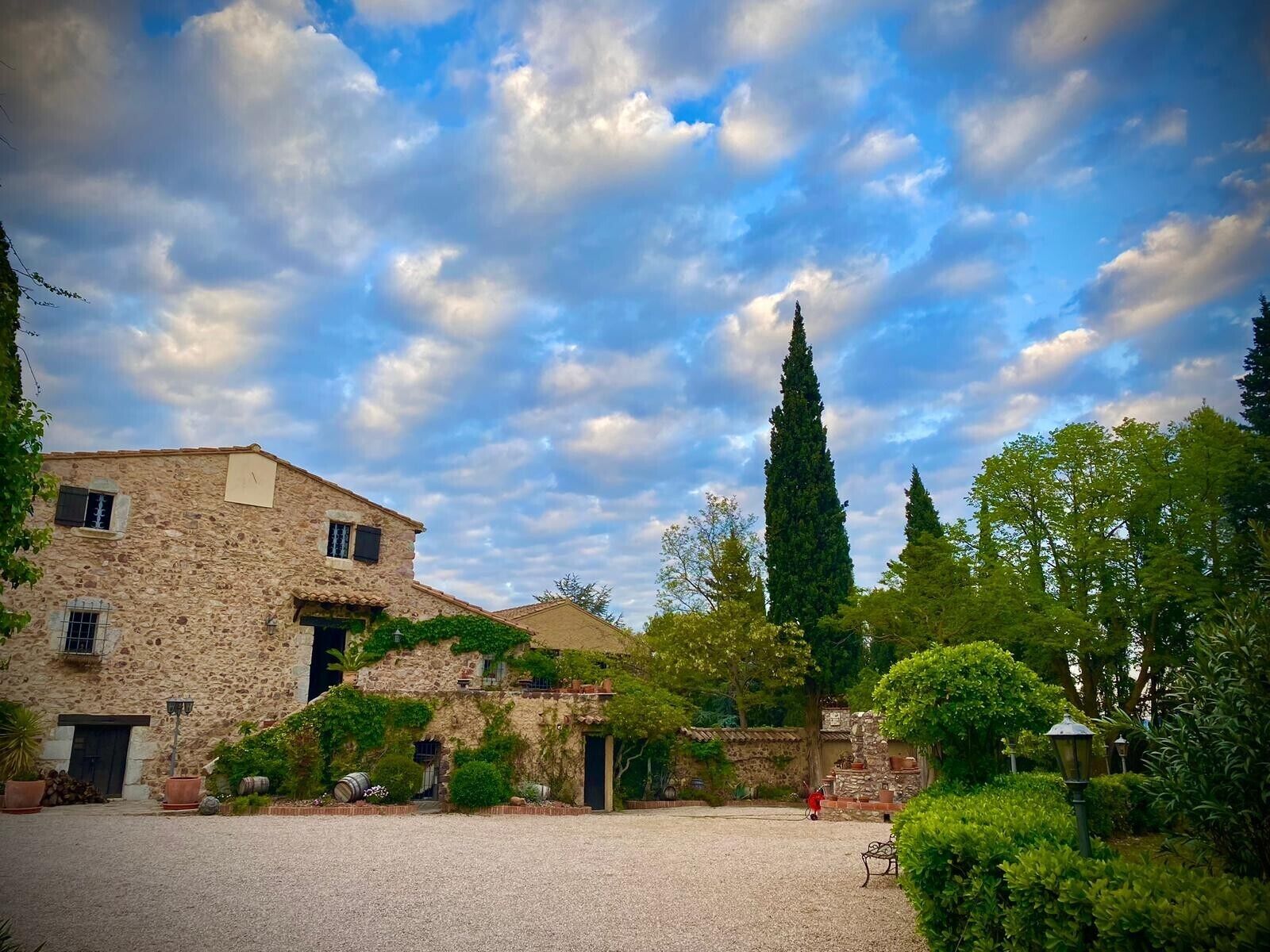 Un edificio de piedra con un patio, un alto ciprés y un jardín bien cuidado.