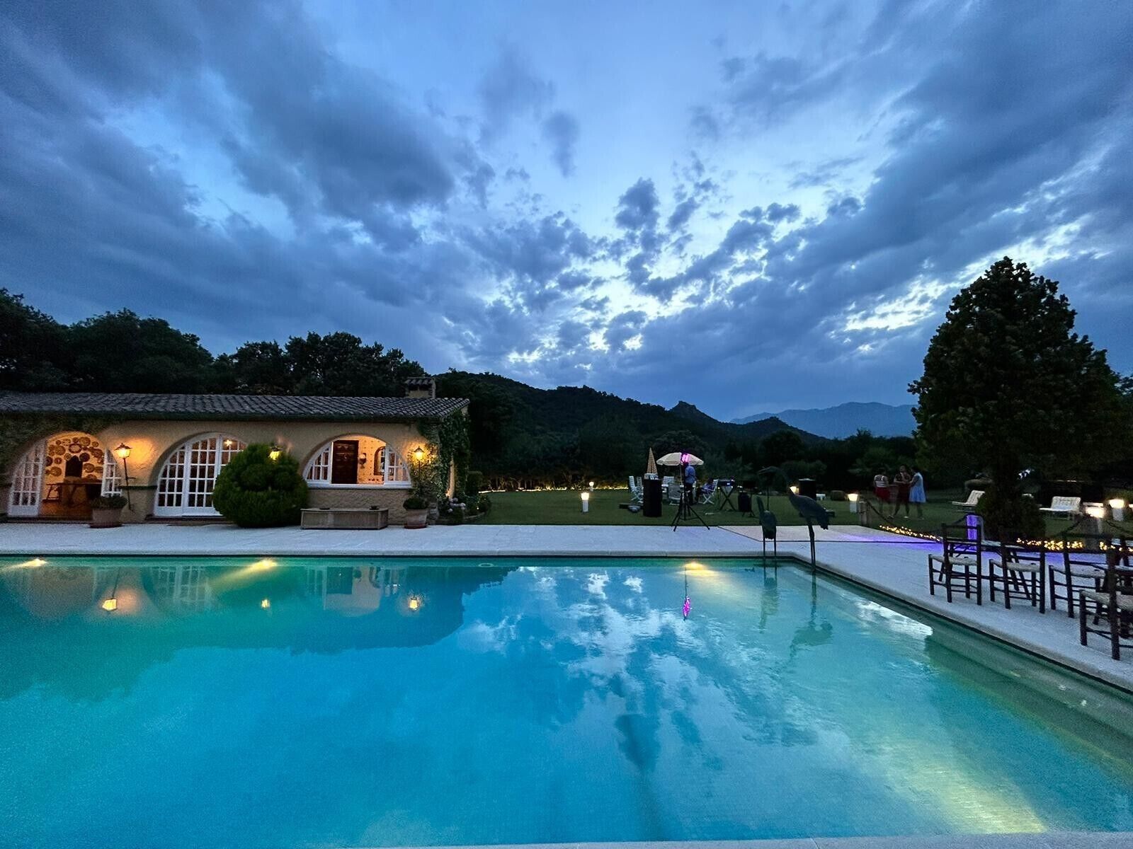 A swimming pool with a building in the background, surrounded by trees and hills.