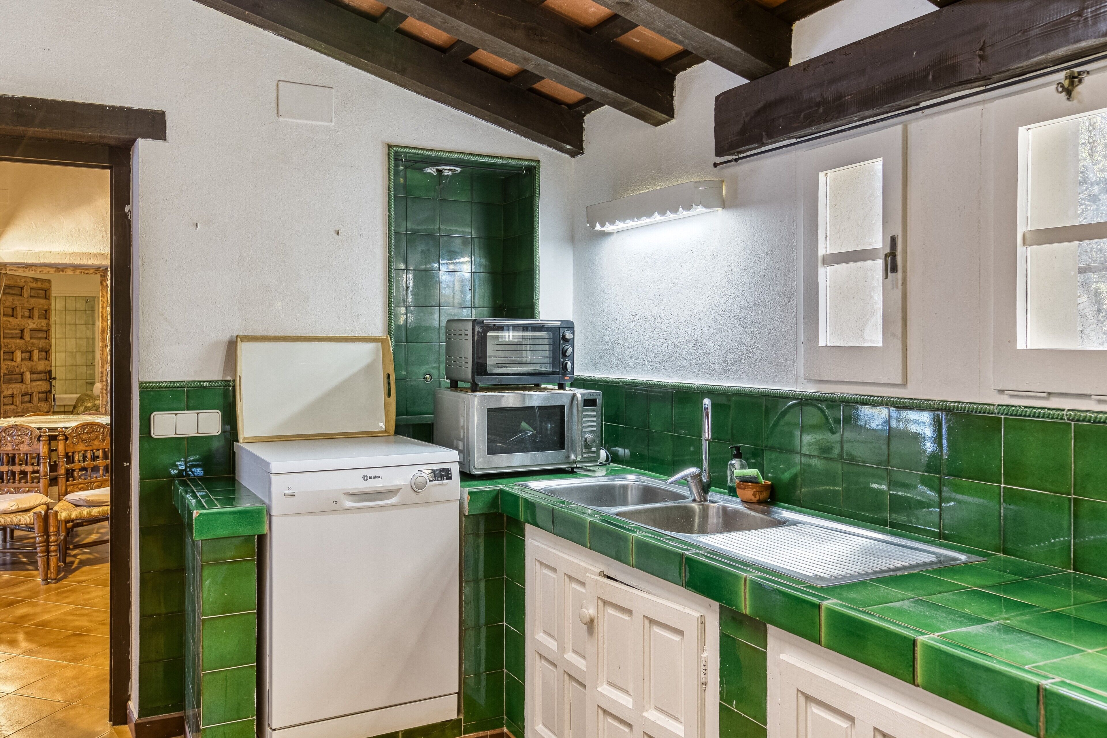 A kitchen with green tiles, a washing machine, a microwave, and a sink.