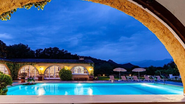 Une piscine avec des chaises longues et un bâtiment doté de fenêtres en arc de cercle.