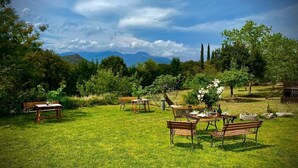 Un espace extérieur aménagé avec des tables et des bancs, entouré de verdure et d’arbres, avec une vue sur les montagnes en arrière-plan.