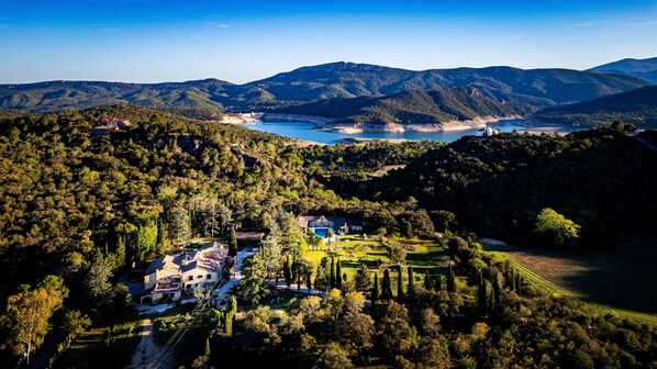 A mountainous landscape with a coastal area, a large house with multiple buildings, and a clear blue sky.