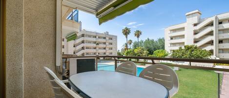 A balcony with a table and chairs, overlooking a swimming pool and adjacent buildings.