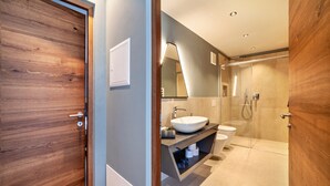 A modern bathroom with a wooden door, a sink, a toilet, and a shower area. - Apartment "Lodge Terrace Exclusive One" with Mountain View & Wi-Fi (Sankt Martin in Passeier)