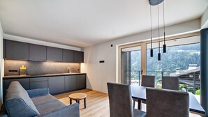 A modern kitchen with grey cabinets, a dining area with a table and chairs, and a large window offering a view of a forested area. - Apartment "Lodge Terrace Exclusive One" with Mountain View & Wi-Fi (Sankt Martin in Passeier)