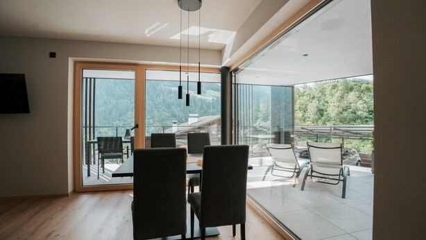 A modern interior with a dining area, large sliding glass doors to a balcony, and a view of a mountainous landscape. - Apartment "Lodge Terrace Exclusive One" with Mountain View & Wi-Fi (Sankt Martin in Passeier)