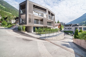 Ein modernes Mehrfamilienhaus mit Balkonen, einer Steinsichtmauer und einem gepflasterten Einfahrt.