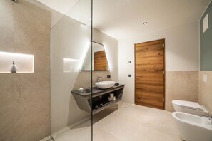 Un baño moderno con cabina de ducha de vidrio, una bañera independiente, una puerta de madera y un tocador empotrado con espejo.
