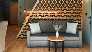 A modern living room with a grey sofa, a wooden side table, and a geometric wooden partition. - Studio Apartment 'Garden Lodge Exclusive Two' with Mountain View, Private Terrace and Wi-Fi (Sankt Martin in Passeier)