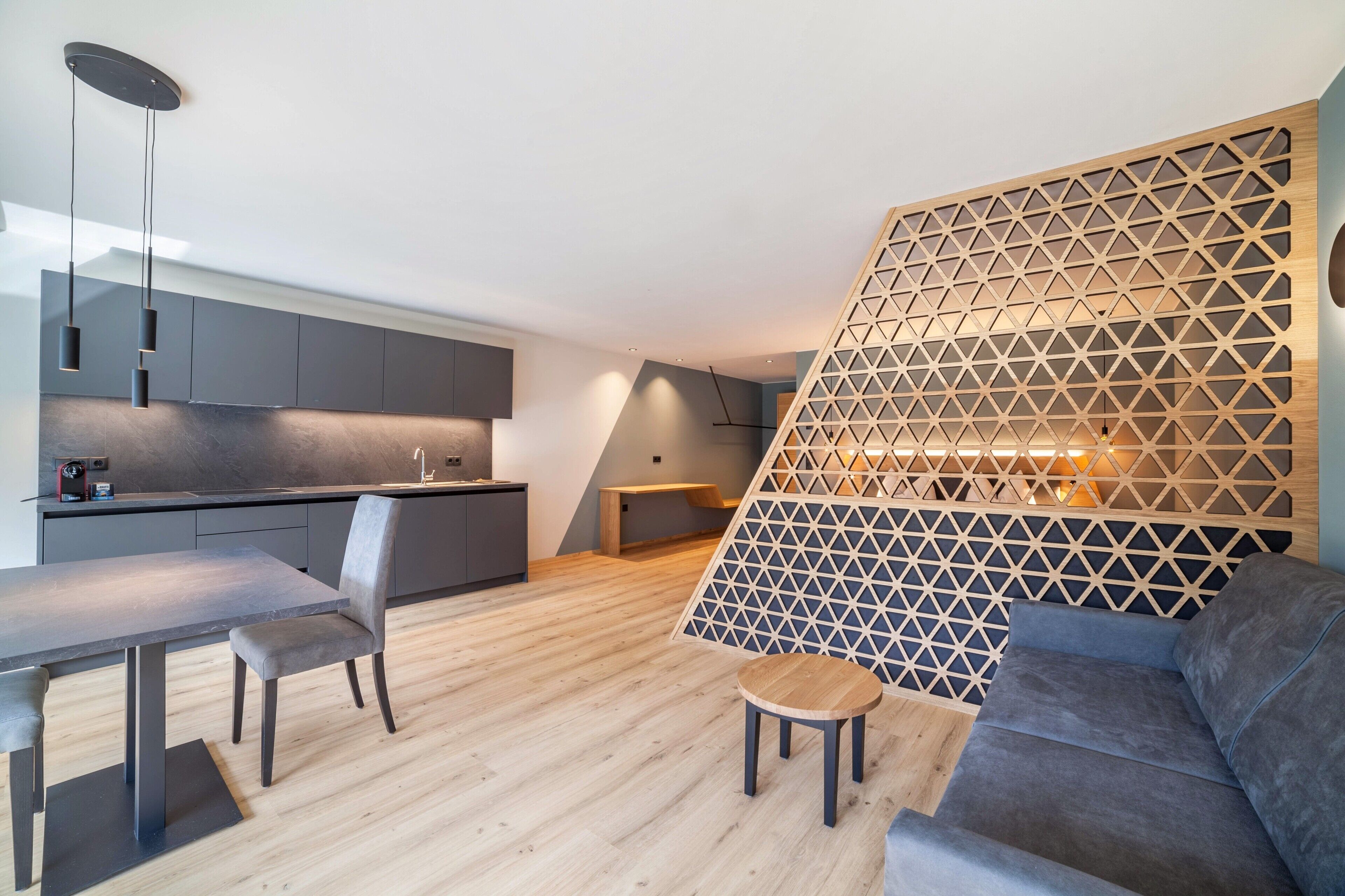 A modern kitchen with dark cabinets, a dining table, and a wooden partition with a geometric pattern.