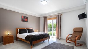 Un dormitorio con cama, mesita de noche, silla y televisor en la pared.
