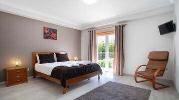 Un dormitorio con cama, mesita de noche, silla y televisor en la pared.
