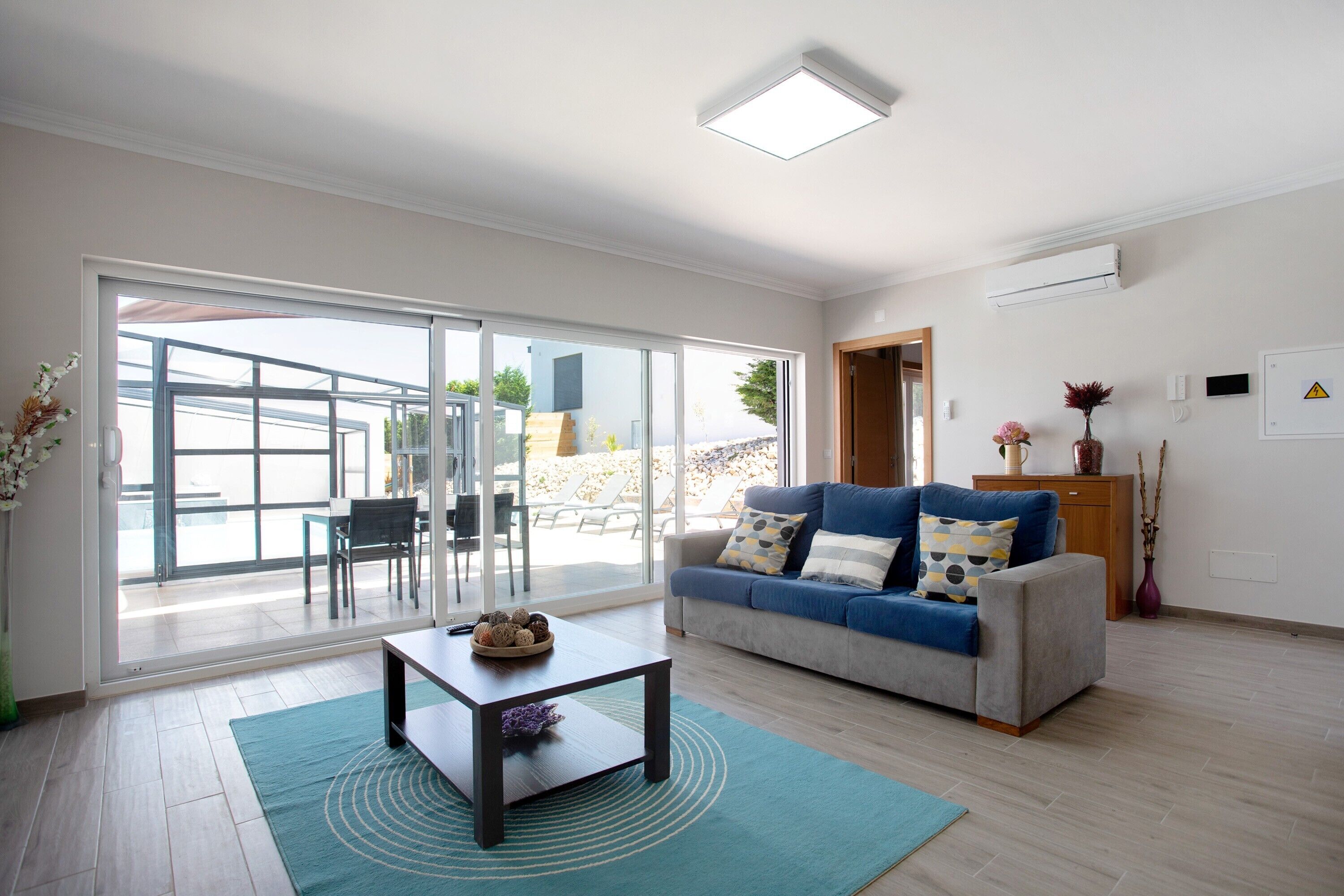 Una sala de estar moderna con sofá, mesa de centro y un amplio ventanal corredera que da a un espacio exterior.