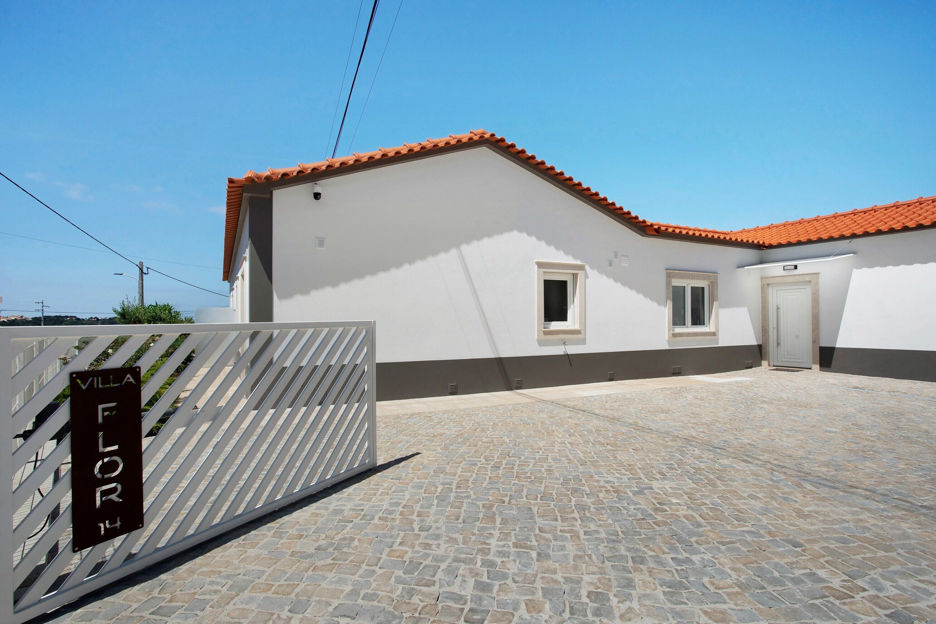 Una villa con techo de tejas, patio empedrado y entrada protegida por una reja.
