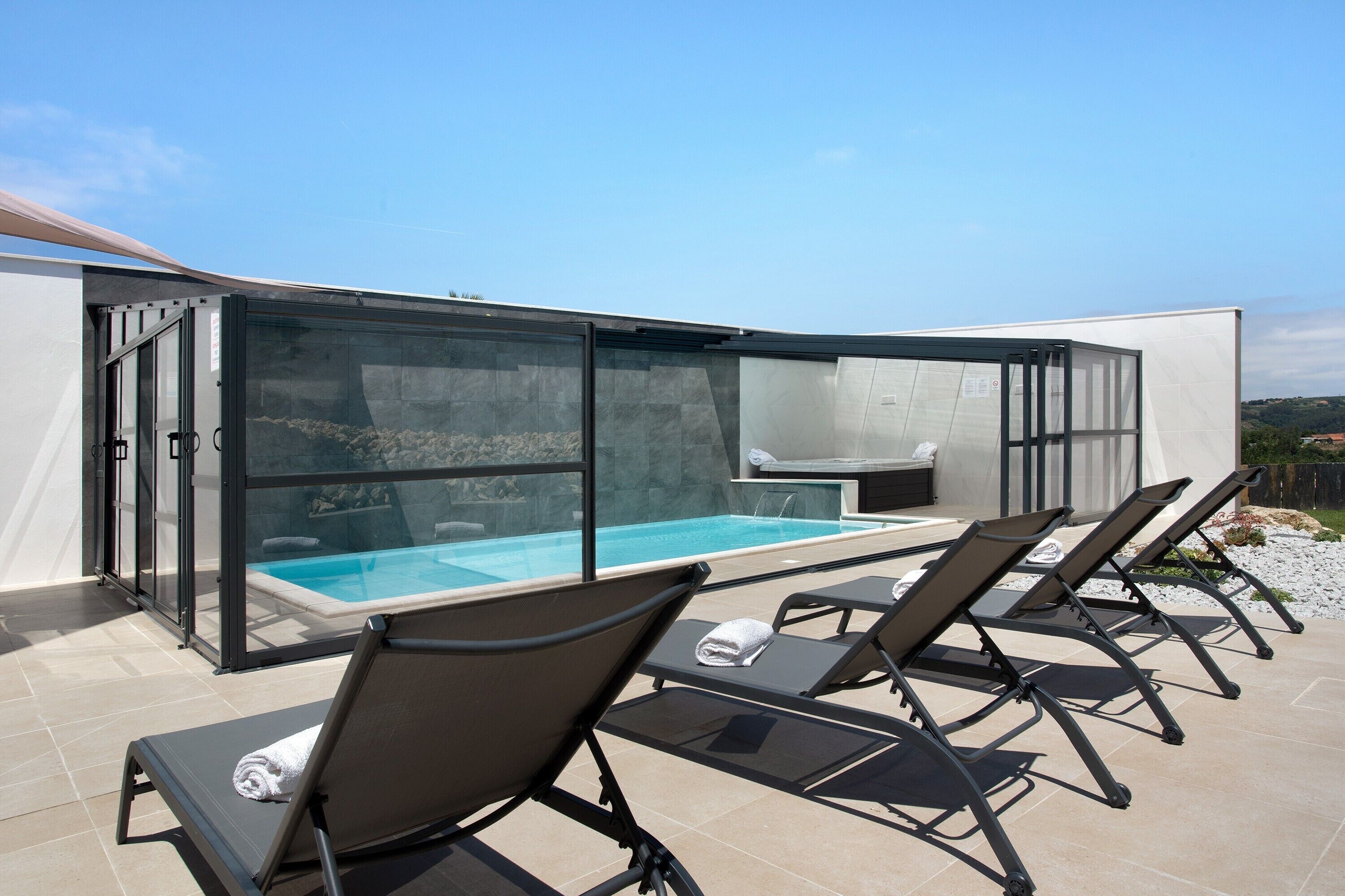 A modern outdoor pool area with glass walls, lounge chairs, and a stone wall backdrop.