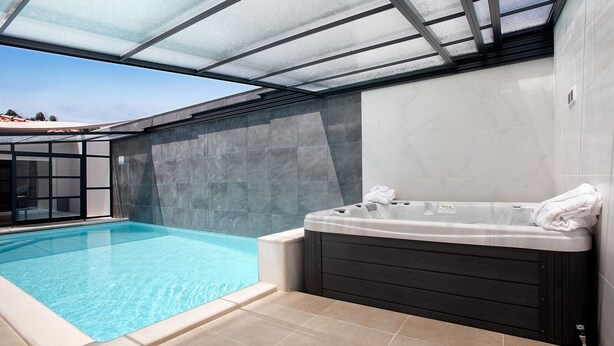 Una piscina junto a un jacuzzi con techo de cristal.