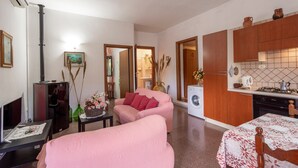 Ett kompakt bostadsutrymme med en soffa, ett litet bord, en tv, en tvättmaskin och ett köksutrymme.