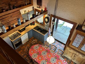 A kitchen with a gas stove, sink, and wooden cabinets. There is a dining table with chairs and a patterned tablecloth.