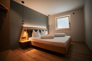 A bedroom with a wooden bed, a bedside table, a hanging light, and a window.