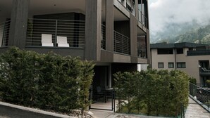 A modern multi-story building with balconies, a staircase, and a paved area with small trees. - Apartment "Lodge Terrace Exclusive Large" with Mountain View & Wi-Fi (Sankt Martin in Passeier)