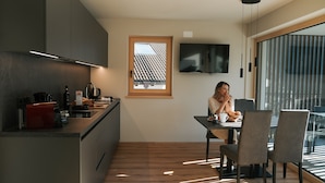 A modern kitchen with a dining area, a TV mounted on the wall, and a window with blinds. - Apartment "Lodge Terrace Exclusive Large" with Mountain View & Wi-Fi (Sankt Martin in Passeier)