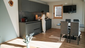 A modern kitchen with dark cabinets, a wooden cutting board, and a person preparing food. - Apartment "Lodge Terrace Exclusive Large" with Mountain View & Wi-Fi (Sankt Martin in Passeier)